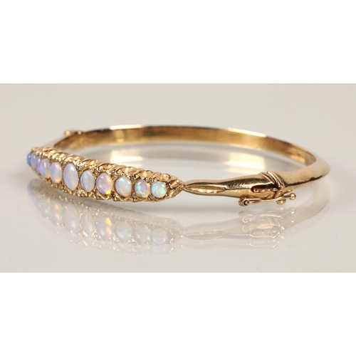 71 - 9ct yellow gold stiff bangle set with eleven graduated opals, 6.5cm diameter, 15.3 grams.