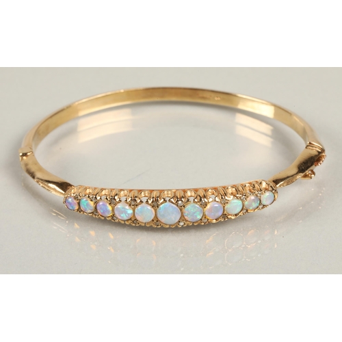 71 - 9ct yellow gold stiff bangle set with eleven graduated opals, 6.5cm diameter, 15.3 grams.