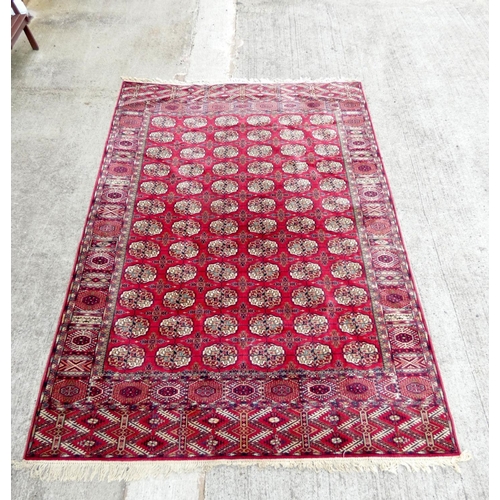 394 - Vintage machine made wool Bokhara rug having six rows of twelve medallions. 248cm x 344cm.