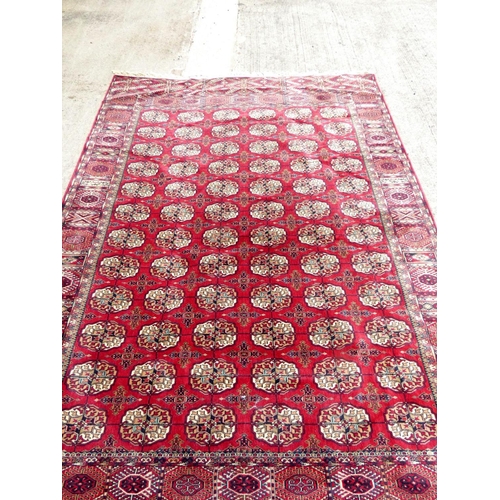 394 - Vintage machine made wool Bokhara rug having six rows of twelve medallions. 248cm x 344cm.