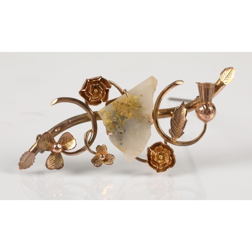 65 - Yellow metal brooch with elaborate floral design, set with a piece of likely quartz with pyrite incl... 