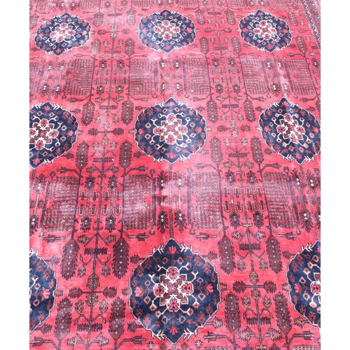 942 - Large Afghan tribal carpet with blue floral lozenges on a red ground, 370cm x 285cm.