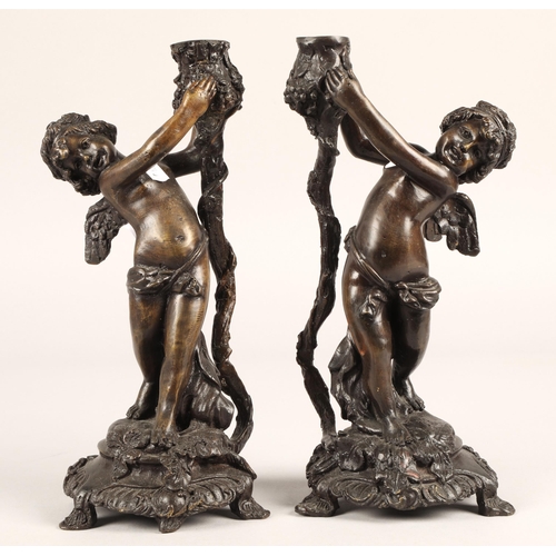 29 - Pair of Bronzed metal putti each holding aloft a candle holder on stylised base, 29cm h...