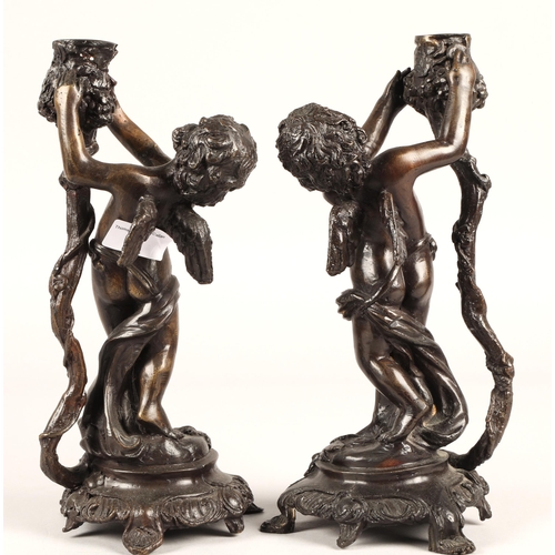 29 - Pair of Bronzed metal putti each holding aloft a candle holder on stylised base, 29cm h...