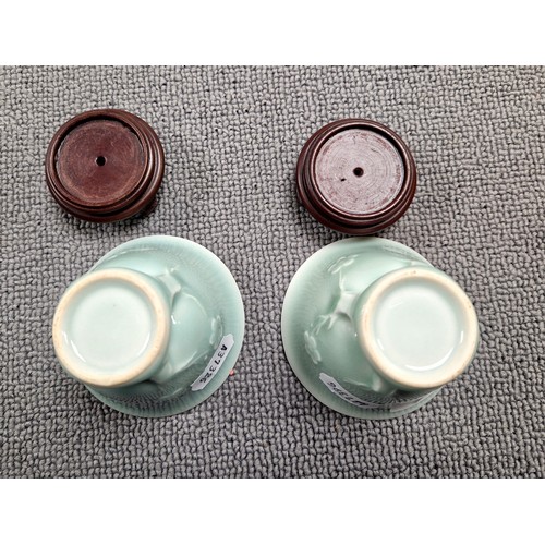 31A - Pair of Oriental celadon glaze ceramic cups on on wooden stands, each cup approx 6cm (not including ...