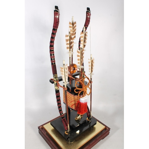 1 - Cased display of a pair of Japanese recurved short bows with arrows, 87cm high.