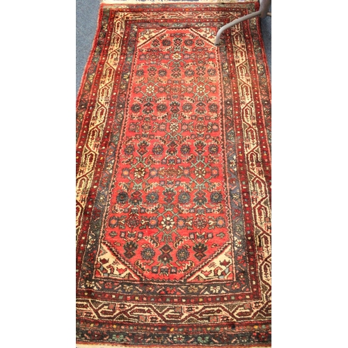 694 - Red ground multi bordered fringed rug with floral decoration, 214cm x 111cm.