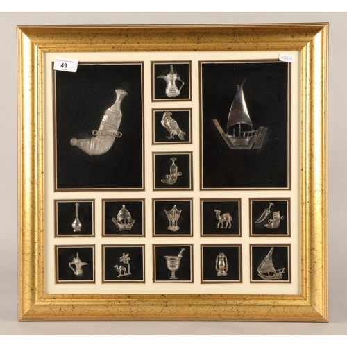 49 - Framed group of white metal trinkets to include dagger, boat is stamped sterling