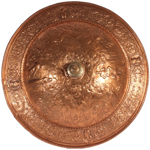In the manner of Elkington & Co.; a Victorian copper parade shield, the gadrooned rim around acanthus scrolled border with embossed mask vignettes, the convex body finely relief decorated and engraved with scenes of St. George and the Dragon, Hercules and the Minotaur, masks and scrolls, centred by a protruding brass spike, W68cm.