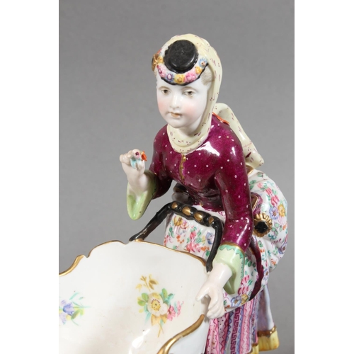 213 - Continental novelty porcelain cream boat in the form of a female flower seller pushing a three wheel... 