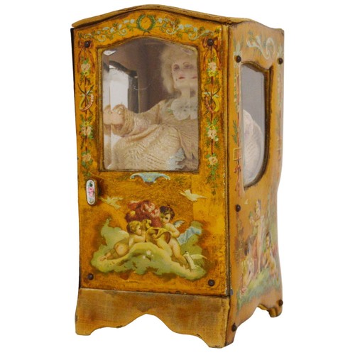 Antique French composition doll enclosed in a model display case in the form of a carriage, decorated with relief putti, and two china tea cosy finials.