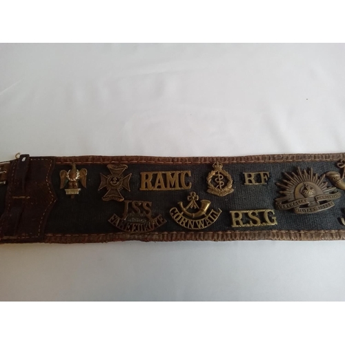 37 - Military belt with cap & collar badges attached. 27 badges in total