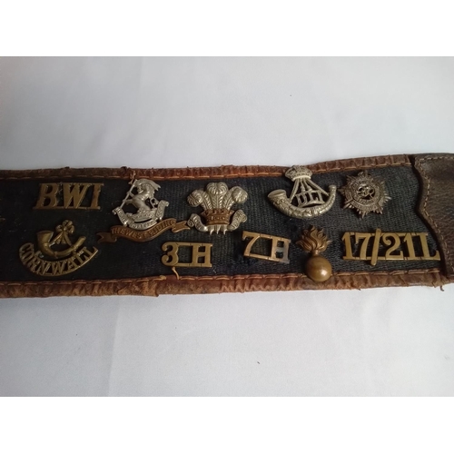 37 - Military belt with cap & collar badges attached. 27 badges in total