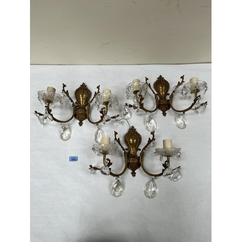 225 - A set of three gilt metal twin branch wall lights, hung with teardrop prismatic drops. Each 12' high... 