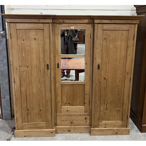 392 - A pine inverted break fronted triple wardrobe with centre mirrored door and fitted drawer. 72