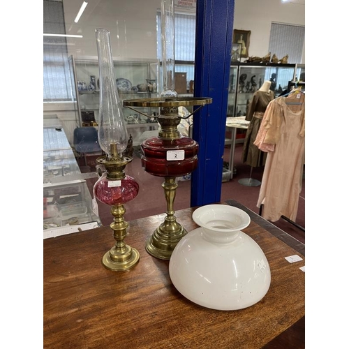 2 - Victorian oil lamps brass bases, red glass reservoirs, one with white shade. 23½ins. and 20ins. (2)