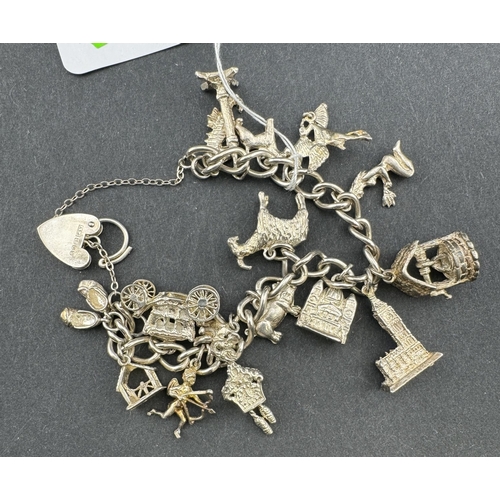 839 - Jewellery: A silver curb link bracelet with heart clasp, hung with in excess of fifteen charms inclu... 