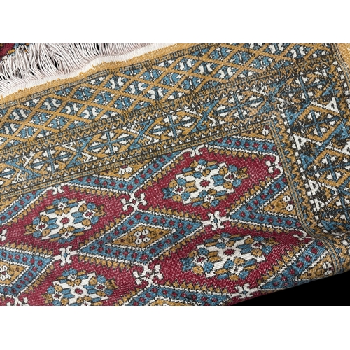 6 - Rugs: a 20th C Bokhara rug, deep red diamonds within a light brown and blue border, approximately 14... 
