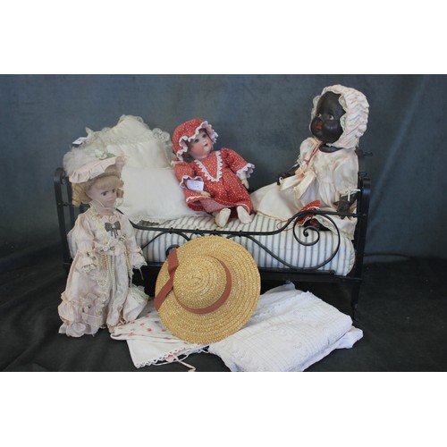 305 - A wrought iron dolls bed, 62cm long, together with bedding, and three dolls.