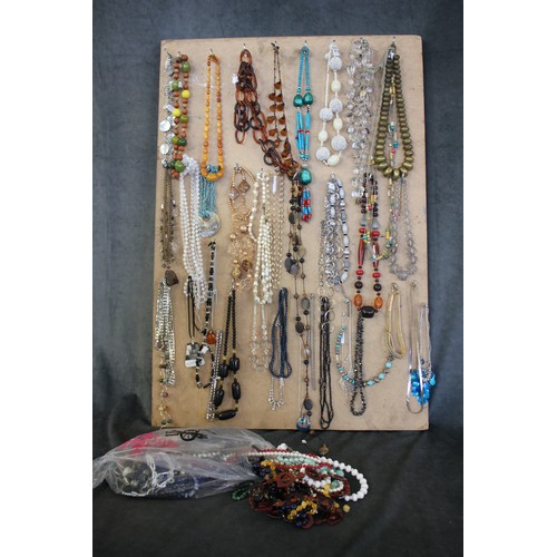 344 - A quantity of costume necklaces, mounted on a board, including a simulated amber necklace, and a sma... 