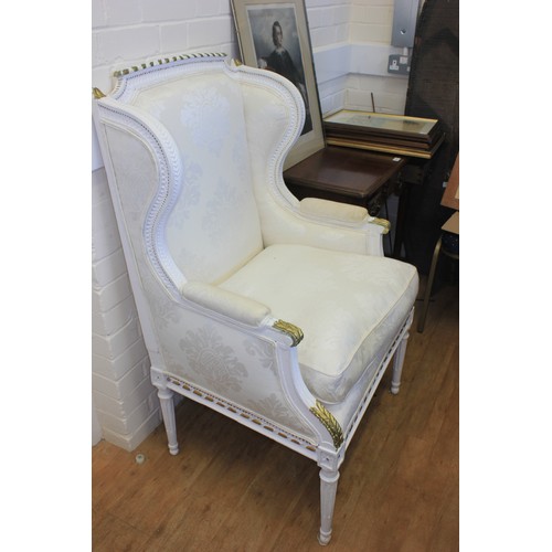 294 - A white and gilt 18th century style winged armchair, on turned and fluted legs.