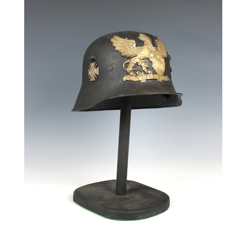 1128 - A trench art German helmet on stand mounted with helmet plate and badges.