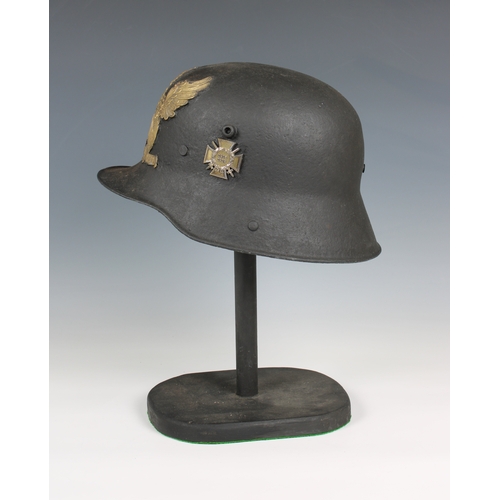 1128 - A trench art German helmet on stand mounted with helmet plate and badges.