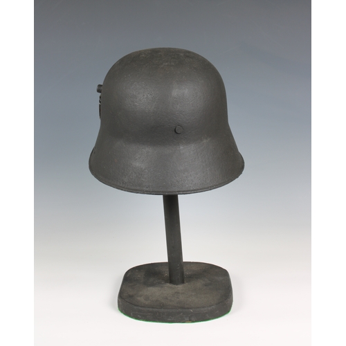 1128 - A trench art German helmet on stand mounted with helmet plate and badges.