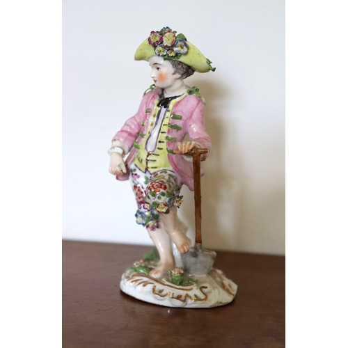 369 - A Sitzendorf porcelain figure of a boy gardener with one foot on his spade, wearing a yellow waistco... 