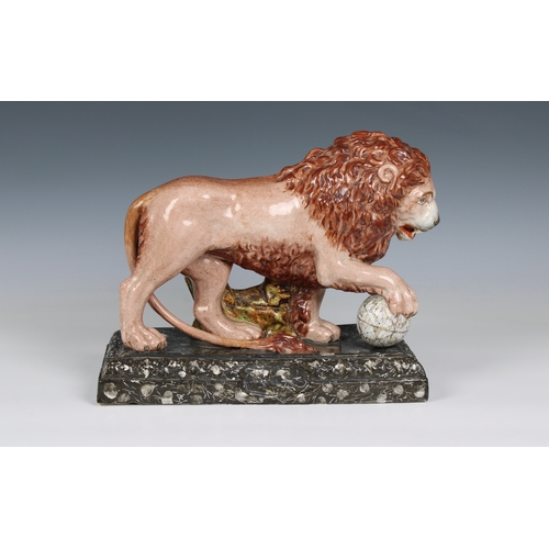 401 - An early 19th century Staffordshire pottery figure of a lion with a paw on a globe, modelled on one ... 