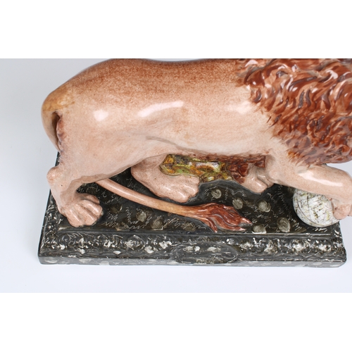 401 - An early 19th century Staffordshire pottery figure of a lion with a paw on a globe, modelled on one ... 