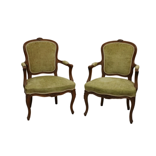 560 - A pair of French beechwood channel carved open armchairs upholstered in green velvet, with floral ca... 