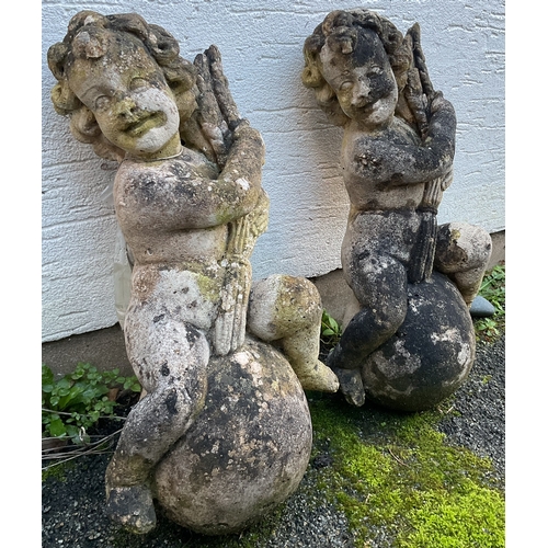 577 - A pair of composite stone Putti each depicting a figure raised on a sphere holding aloft a sheaf of ... 