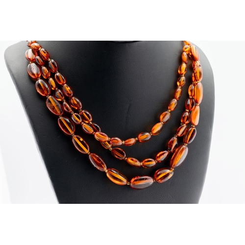 1127 - A vintage polished amber necklace, having triple rows to bottom the beads of irregular shapes and si... 