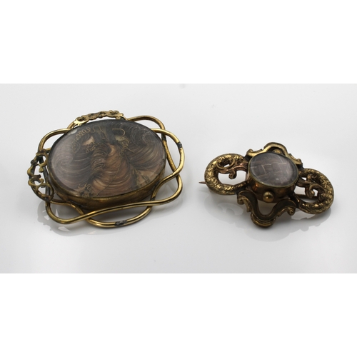 1193 - Two Victorian mourning hair art brooches each of shaped form with central glazed panels of hair, the... 