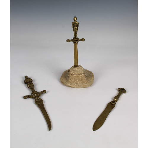 1381 - Three brass paper knives one of figural form, having stone effect stand with applied military badges... 