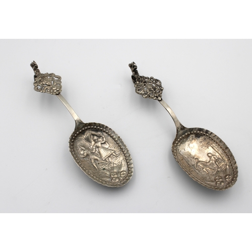 1039 - A pair of large Dutch silver wine or fruit spoons repousse decorated with figures in town scenes, sq... 