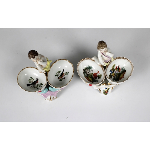 25 - A pair of 20th century KPM, Germany, porcelain salts, each featuring a putti with two baskets in pol... 