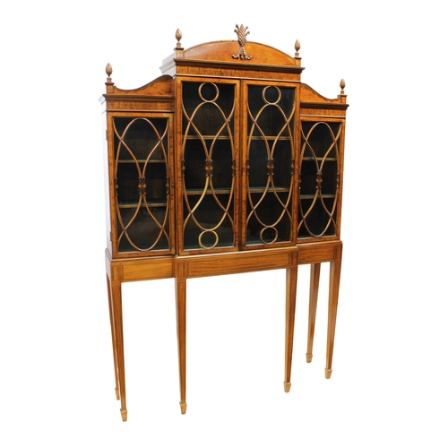 64 - A satinwood breakfront cabinet on standin the Sheraton style, with four glazed doors enclosing shelv... 