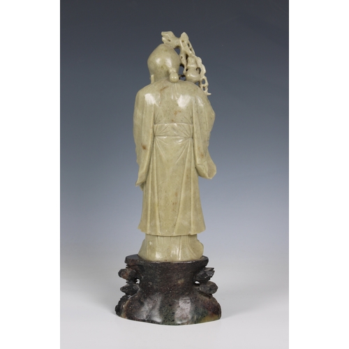 814 - A finely carved celadon soapstone Chinese figurecarrying a peach and holding a staff, standing on a ... 