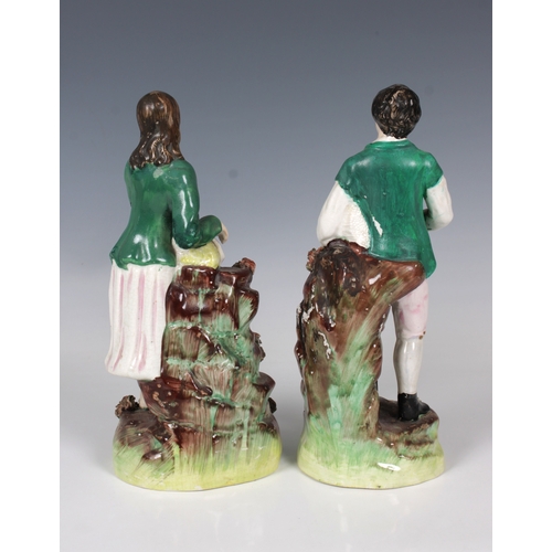 2075 - A pair of 19th century Staffordshire ceramic figures of a young country couple, each wearing a green... 