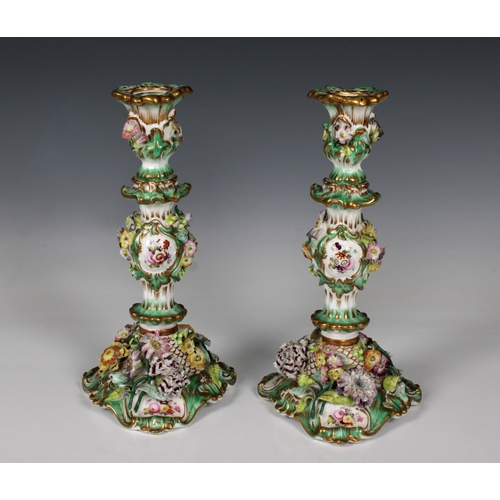 2120 - A pair of Continental porcelain candlesticks, with a green ground encrusted with hand painted applie... 