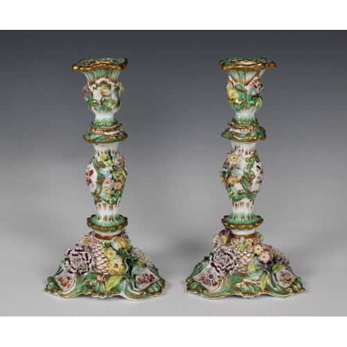 2120 - A pair of Continental porcelain candlesticks, with a green ground encrusted with hand painted applie... 