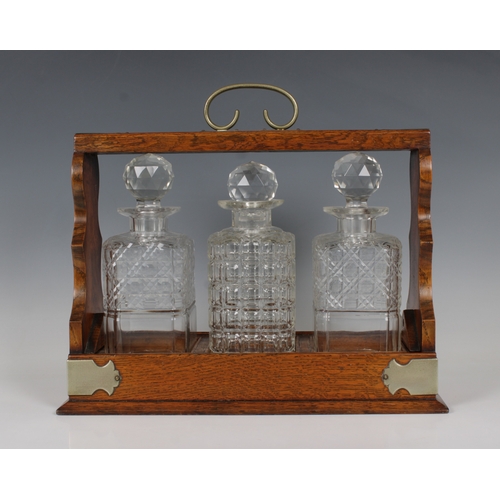 108 - An oak three bottle tantalus of typical form, holding un-matched crystal decanters.