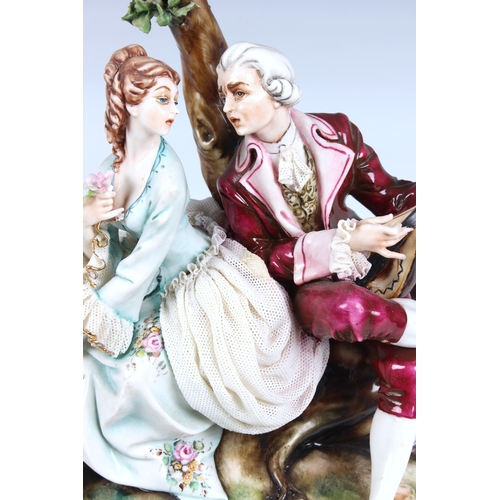 265 - A Capodimonte figure of a courting couple in 18th century costume, seated beneath a tree, the gentle... 