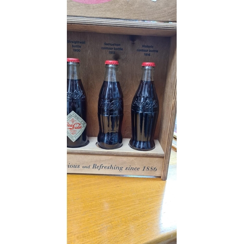 58 - Set of 4 Historic Coca Cola Bottles in a Wooden Display Cabinet. released c.2012