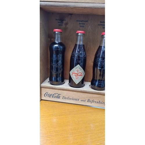 58 - Set of 4 Historic Coca Cola Bottles in a Wooden Display Cabinet. released c.2012