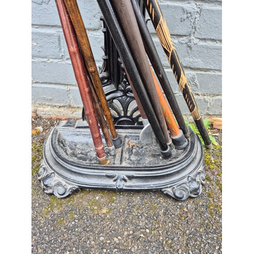 101 - A collection of antique and vintage walking sticks in an ornate cast iron stand to include a duck-he... 