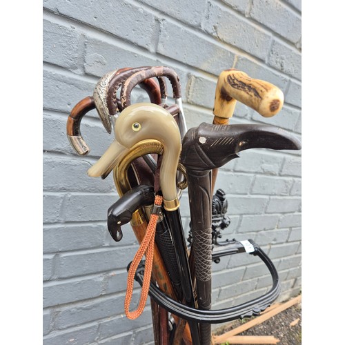 101 - A collection of antique and vintage walking sticks in an ornate cast iron stand to include a duck-he... 