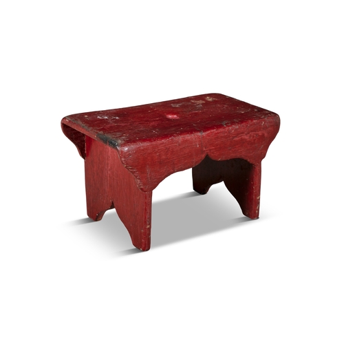 93 - A RED PAINTED PINE LOW RECTANGULAR STOOL  with shaped apron on panel end supports. 25cm high, 44cm w... 